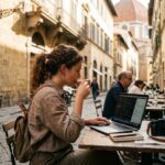 A laptop, camera, and passport on a desk overlooking a scenic view representing getting paid to travel.